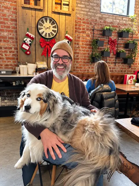 Smiling guest with an Australian shepherd on his lap, holiday decor on the brick wall.