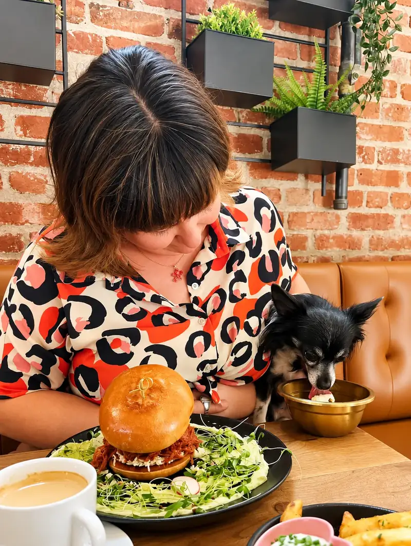 Cliente avec un burger au porc effiloché pendant que son chihuahua noir mange dans un bol doré